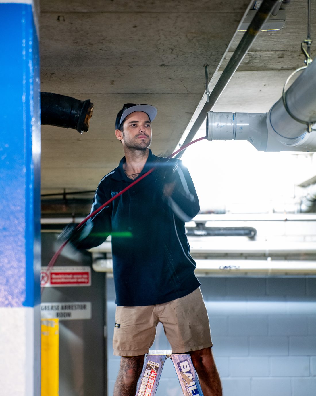 Cooly plumber working from a ladder on overhead pipework